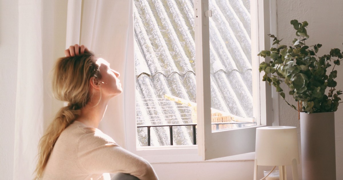 Femme installée près d'une fenêtre dans la lumière douce du matin, un moment de calme pour préparer la rentrée avec layoga thérapie